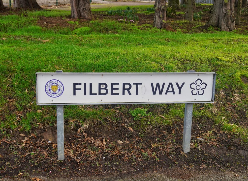 Leicester, UK, February 15, 2026: A white street sign for Filbert Way featuring the Leicester City Football Club crest and a floral emblem outside the King Power Stadium.